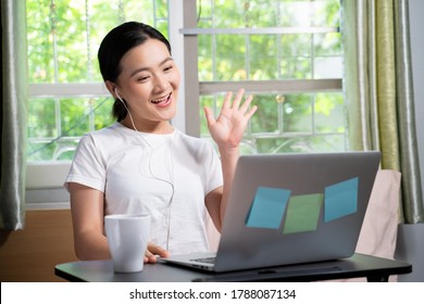 Asian Woman With Earphone Happy Meeting By Video Call With Laptop Sitting On The Bed At Home. WFH. Work From Home. Social Distancing Concept.