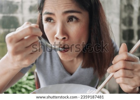 Asian woman eat spicy noodles with chopsticks in local street.