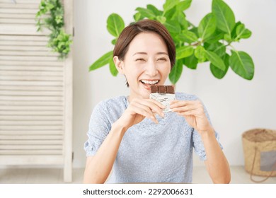 Asian woman eating chocolate bar at home - Powered by Shutterstock