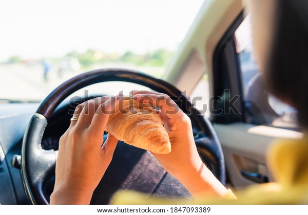 Asian woman eating food fastfood while driving\
the car in the morning during going to work on highway road,\
Transportation and vehicle\
concept
