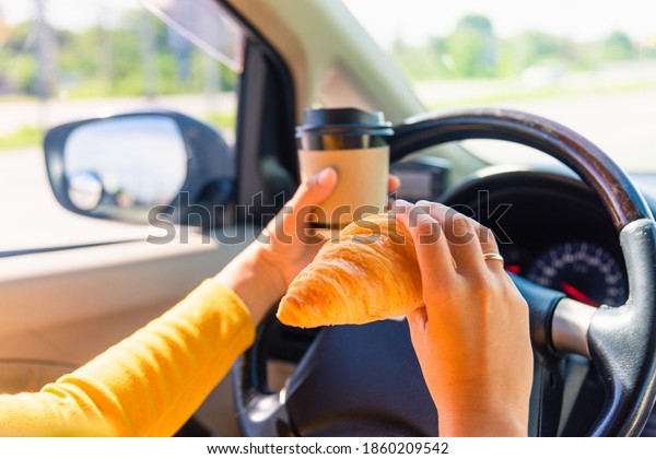 Asian woman eating food fastfood and\
drink coffee while driving the car in the morning during going to\
work on highway road, Transportation and vehicle\
concept
