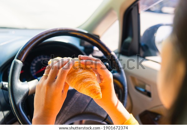 Asian woman eating food fastfood while driving\
the car in the morning during going to work on highway road,\
Transportation and vehicle\
concept