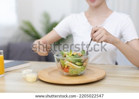 Asian woman eating salad on the dining table smiling and happy, Vegetable salads are rich in vitamins and minerals, Fat-low-calorie and high-fiber diets, Health care by eating fresh vegetables.