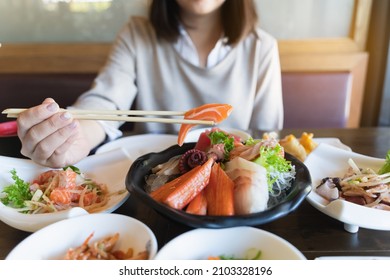 Asian Woman Eating A Sashimi Salmon. Woman Using Chopstick To Pick Raw Fish Sashimi From White Bowl.