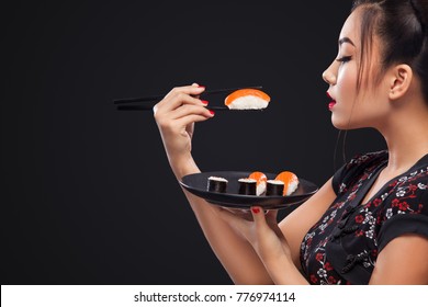 Asian Woman Eating Sushi And Rolls On A Black Background.