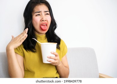 Asian woman eating very hot and spicy noodle from a cup her mouth and tongue burning and red  - Shutterstock ID 1998439778