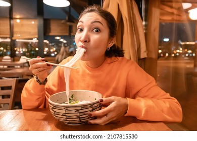 Asian Woman Eating Vietnamese Noodle Soup Using Chopsticks In Restaurant