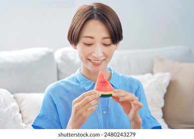 Asian woman eating the watermelon in the living room - Powered by Shutterstock