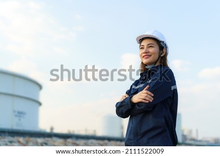 Asian woman engineer arm crossed and smile with confident looking forward to future with oil refinery plant factory in background. 