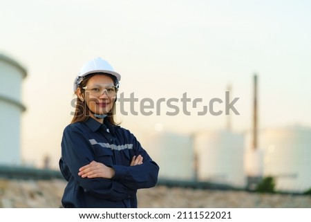 Asian woman engineer arm crossed and smile with confident looking forward to future with oil refinery plant factory in background. 