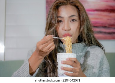 Asian Woman Enjoy Eating Hot Instant Noodles Alone In The Living Room After House Work. Young Freelance Female Work From Home.