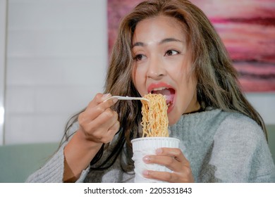 Asian Woman Enjoy Eating Hot Instant Noodles Alone In The Living Room After House Work. Young Freelance Female Work From Home.