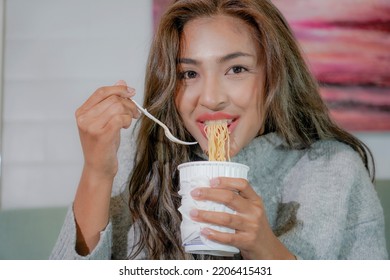 Asian Woman Enjoy Eating Hot Instant Noodles Alone In The Living Room After House Work. Young Freelance Female Work From Home.