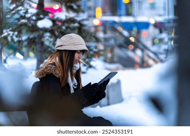 Asian woman enjoy urban outdoor lifestyle remote working on digital tablet with internet for freelance work or searching online map direction during travel in the city waiting for bus in winter night. - Powered by Shutterstock