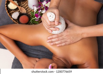Asian woman enjoying compress balls, herbal ball massage at spa.