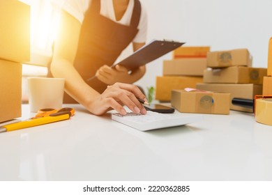 Asian Woman, Entrepreneur, Small Business, SME, Independent, Press The Calculator To Account For Customers Who Order. And Check The Purchase Order Invoice Prepare Parcels For Delivery.