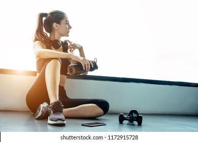 Asian woman exercising in the gym, Young woman workout in fitness for her healthy and office girl lifestyle. She using smart phone to check an email or listening music.