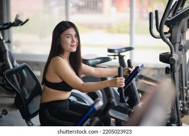 Asian Woman Exercising On A Bicycle In The Gym, Smiling To Lose Weight, Makes Her Healthy. Exercise Bike Woman Fitness Sport Concept.