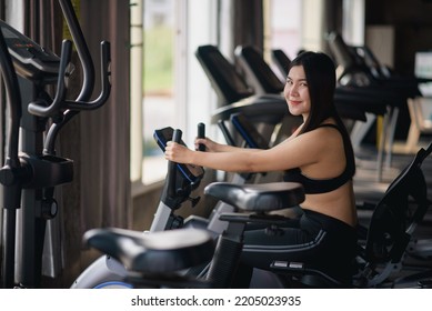 Asian Woman Exercising On A Bicycle In The Gym, Smiling To Lose Weight, Makes Her Healthy. Exercise Bike Woman Fitness Sport Concept.