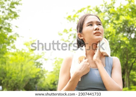 Asian woman exercising outdoors on a hot sunny day with her body temperature above 40 degrees Celsius. She wipes her sweat with a towel. heat stroke concept. copy space