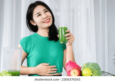 Asian woman experiencing delight and vitality relishes a refreshing blend of green fruits and vegetable juice, embracing its benefits for healthy digestive system, nutrient-rich fiber detoxification  - Shutterstock ID 2306376561
