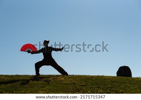 Asian woman with fan practicing taijiquan at sunset, chinese martial arts, healthy lifestyle concept.