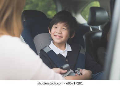 Asian Woman Fastening Child With Safety Seat Belt In Car