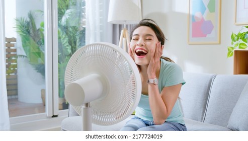 Asian Woman Feel Happy Enjoy Use Modern Fan To Cool Down In Summer Sit On Sofa At Home