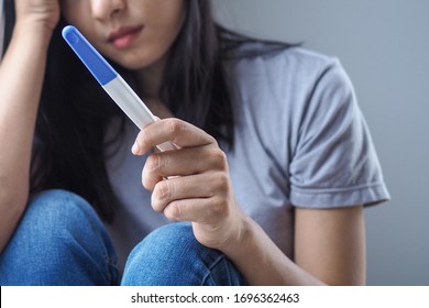 Asian woman feel sad and scare while holding pregnancy test with positive result in bedroom. Unexpected pregnancy and abortion concept