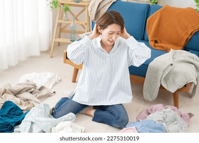 Asian woman feel stress surrounded by clothes at home - Shutterstock ID 2275310019