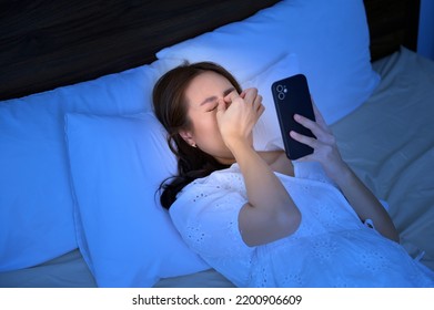 An asian woman feeling eye strain fatigue while using smartphone in bedroom - Shutterstock ID 2200906609