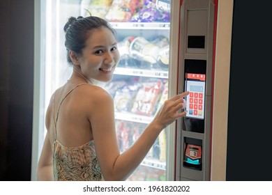 Asian woman feeling happy when using a modern snack vending machine. Her hand touching on vending machine touch screen and looking to the camera. Modern vending machine.