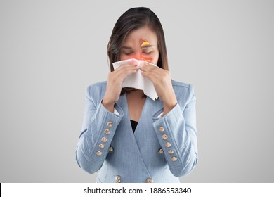 Asian woman feeling unwell because of sinus symptoms on a gray background. Businesswoman in blue suit blowing nose in a tissue. Dust mite allergy. Cold and Flu