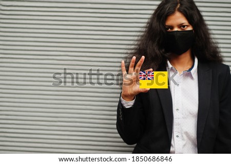 Asian woman at formal wear and black protect face mask hold Niue flag at hand against gray background. Coronavirus at country concept.