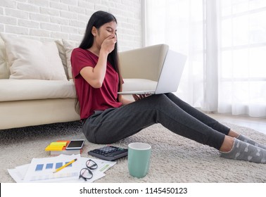 Asian Woman Freelance Yawn While Working On Laptop With Paperwork Sitting One Floor And Leaning Sofa At Home,work At Home Concept