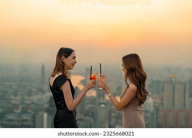 Asian woman friends celebrating dinner party drinking cocktail together at skyscraper rooftop bar in the city at summer sunset. Attractive girl enjoy urban lifestyle nightlife on holiday vacation. - Powered by Shutterstock