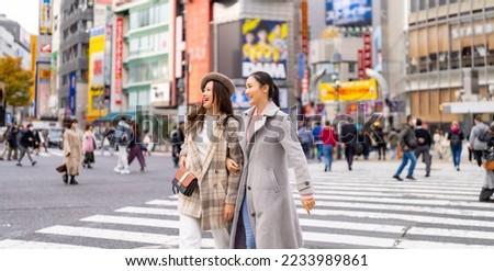 Asian woman friends shopping and crossing street crosswalk with crowd of people at Shibuya, Tokyo, Japan in autumn. Attractive girl  enjoy and fun outdoor lifestyle travel in city on holiday vacation.