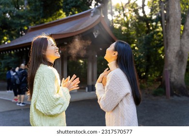 Asian woman friends travel and praying at traditional Meiji Jingu Shrine in Tokyo city, Japan. Attractive girl travel Japan landmark famous place learning Japanese culture in autumn holiday vacation.