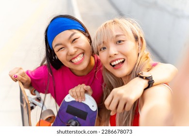 Asian woman friends using mobile phone taking selfie together during skating on longboard skate in the city. Stylish girl have fun outdoor lifestyle skateboarding on city street on summer vacation. - Powered by Shutterstock