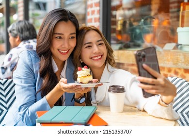 Asian woman friends using smartphone selfie together while sitting at outdoor coffee shop eating bakery and drinking coffee in urban city street. Beautiful female enjoy outdoor lifestyle in the city - Powered by Shutterstock