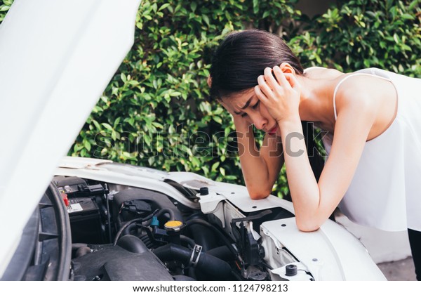 Asian woman frustrated and angry\
checking her broken car and failed engine on roadside\
