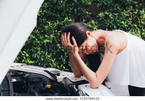 Asian woman frustrated and angry\
checking her broken car and failed engine on roadside\
