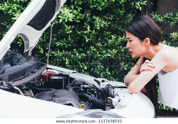 Asian woman frustrated and angry
checking her broken car and failed engine on roadside
