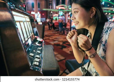 Asian Woman Gambling In Casino Playing On Slot Machines Spending Money. Gambler Addict To Spin Machine. Girl Having Fun Playing Game During Holidays In Las Vegas.