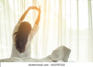 Asian woman get up stretching  relax in bed room at home, early out morning and wake up rest sunny day.  Lifestyle Concept 