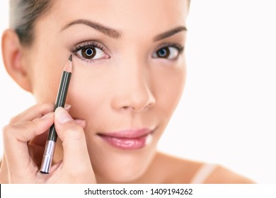 Asian Woman Getting Ready Applying Brown Eyeliner Eye Pencil On Eyes Looking In The Mirror. Isolated On White Background.