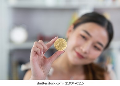 Asian woman girl smiling holding gold bitcoin crypto currency blockchain on wood table desk in living room at home. Crypto currency blockchain Saving investment wealth concept. - Powered by Shutterstock