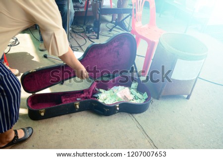 asian woman giving money into the guitar box for the performing of music band at the local street market of Thailand