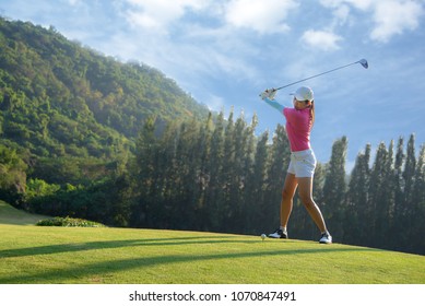 Asian Woman Golf Player Doing Golf Swing Tee Off On The Green Evening Time, She Presumably Does Exercise. Healthy And Lifestyle Concept.