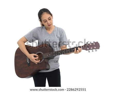 Asian woman in gray t-shirt and black pant playing acoustic guitar. Portrait on white background with studio light.
